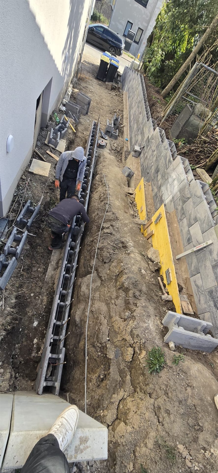 Arbeiter setzen Schalsteine für eine Stützwand neben einem Wohnhaus.