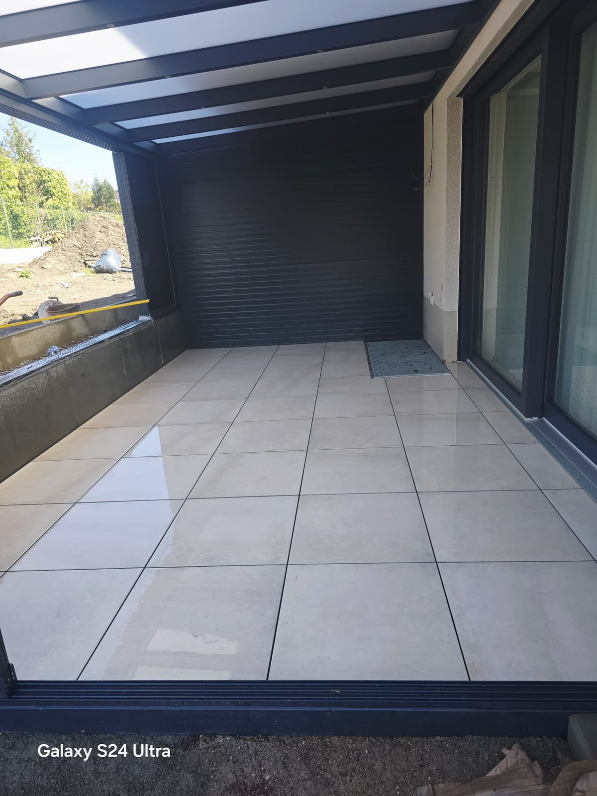 Geflieste Terrasse unter einer dunklen Überdachung.